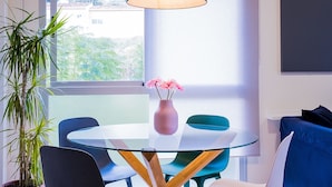 Un comedor moderno con una mesa de vidrio, sillas de madera, un jarrón con flores y una lámpara colgante.