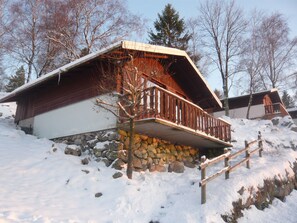 Une cabane en bois avec des fondations en pierre, une terrasse en bois et un mur en pierre.