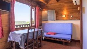 A wooden cabin interior with a dining table, chairs, a sofa, and a window with curtains. - Chalet 'Chalet Les Moraines 8' with Mountain View, Shared Pool and Private Terrace (Le Tholy)
