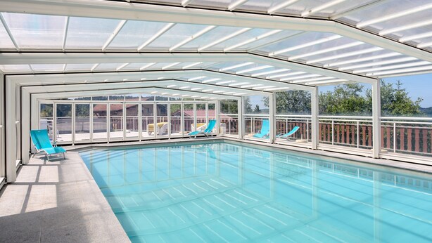 A covered swimming pool with glass walls, blue lounge chairs, and a clear view of the surrounding landscape. - Chalet 'Chalet Les Moraines 8' with Mountain View, Shared Pool and Private Terrace (Le Tholy)