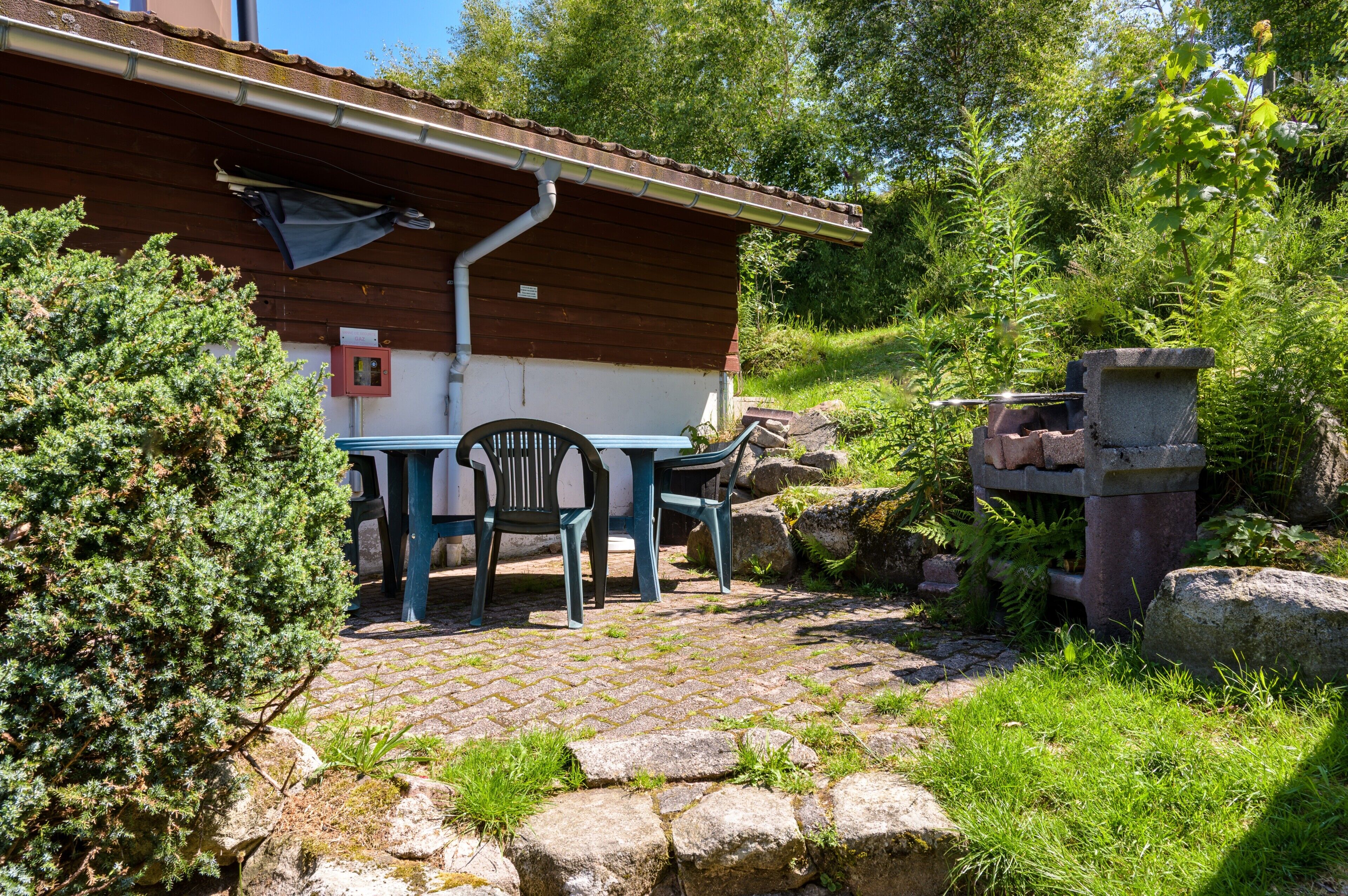 Eine rustikale Holzhütte mit Pflasterterrasse, Sitzgelegenheiten im Freien und einem Kamin aus Stein.