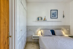 Une chambre à coucher comprenant un lit, des tables de chevet, une commode, une armoire en bois, une étagère avec des objets décoratifs et un tableau encadré au mur.