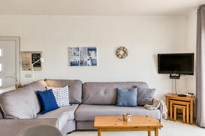 Un salon avec un canapé gris, une table basse en bois, un téléviseur à écran plat et une petite table d’appoint en bois.