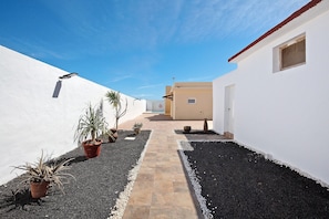 A narrow pathway flanked by white walls, leading to a building with a door and a window.