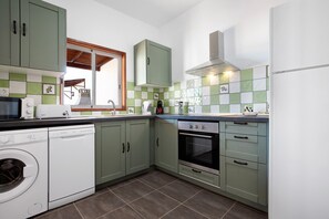A compact kitchen with green cabinets, a built-in oven, a dishwasher, and a washing machine.