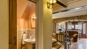 A bathroom with a sink, a towel hanging on the wall, and a staircase leading to a living area with a sofa and a table.