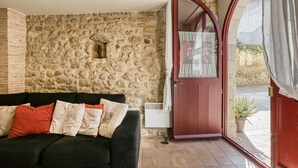 A room with a stone wall, a red door, a black sofa with patterned cushions, and a potted plant outside.