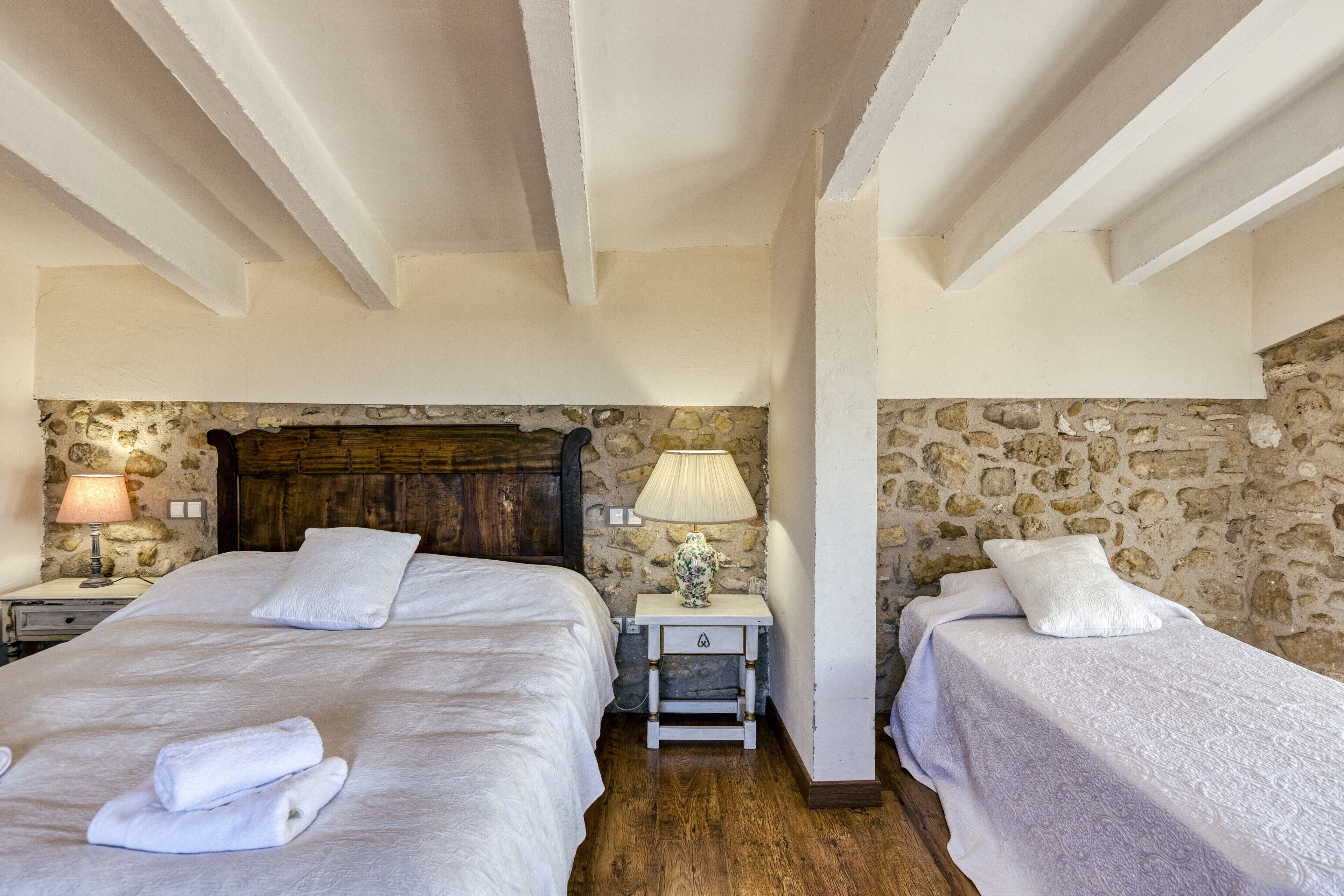 Une chambre avec deux lits, des murs en pierre, des poutres en bois et des lampes de chevet.