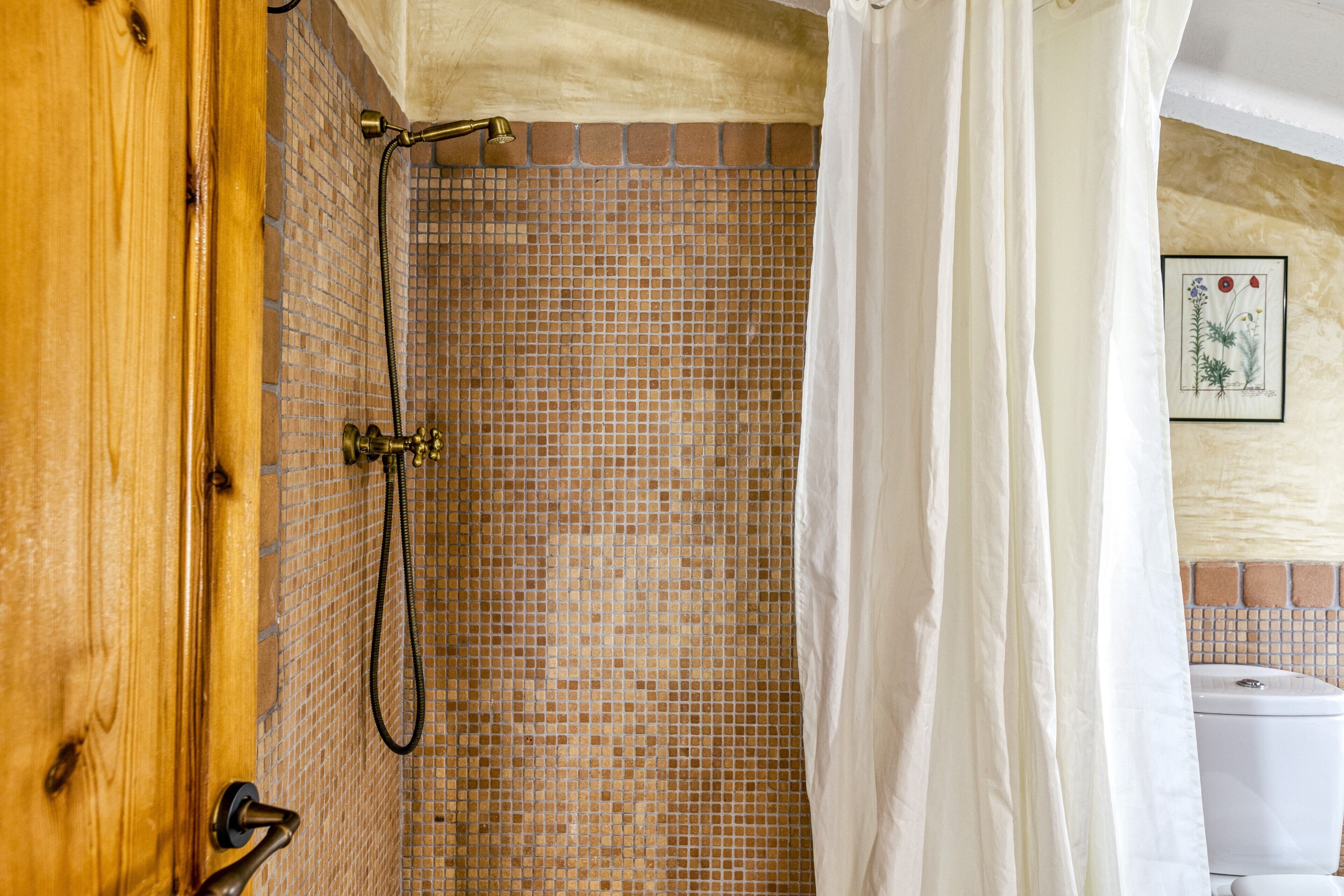 A shower with a tiled wall, a wooden door, and a white curtain.