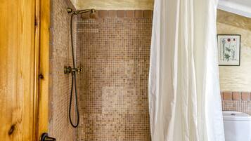 A shower with a tiled wall, a wooden door, and a white curtain.