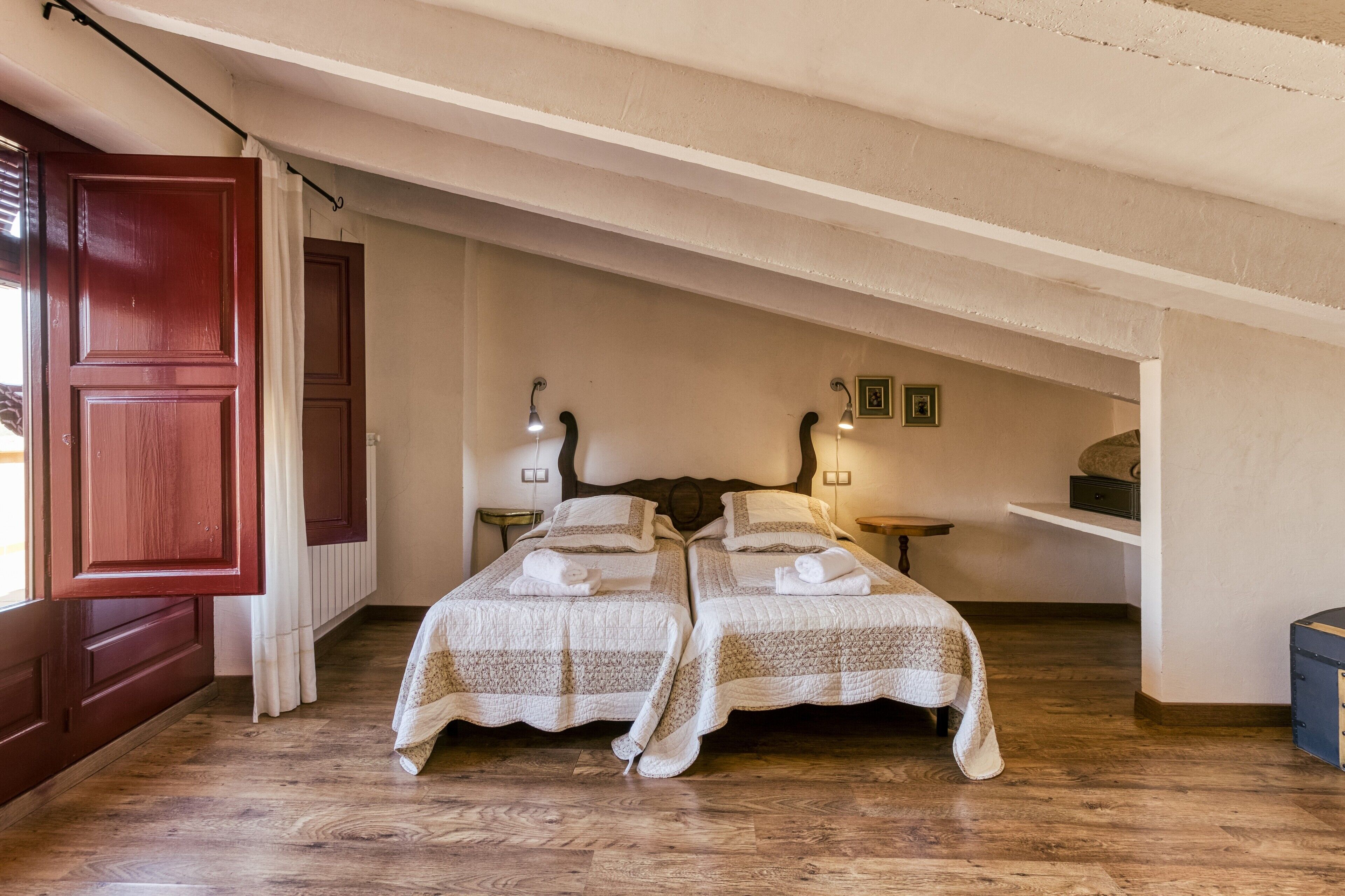A bedroom with two beds, a wooden floor, a red door, and a white ceiling.