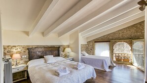 A bedroom with two beds, wooden floors, stone walls, and a balcony with potted plants.