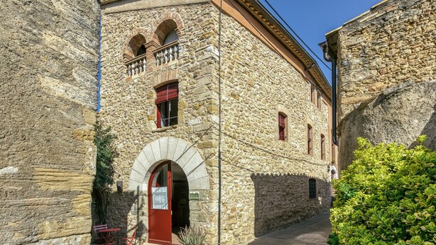 A stone building with a red door, arched windows, and a balcony.