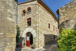 A stone building with a red door, arched windows, and a balcony.