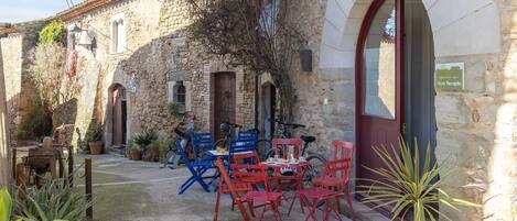 A stone building with a red door, outdoor seating with red and blue chairs, and a bicycle parked outside.