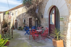 A stone building with a red door, outdoor seating with red and blue chairs, and a bicycle parked outside.