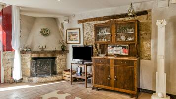 A living room with a fireplace, television, wooden cabinet, and a stone wall.