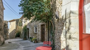 A narrow street with a stone building, a red metal table and chair, and a cat lying on the ground. - Holiday Home 'Vermella' with Wi-Fi (Orriols)