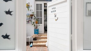 Une porte blanche sur laquelle on peut lire « CASA MAYLIN », un hall d’entrée carrelé et une petite plante en pot posée sur les marches.