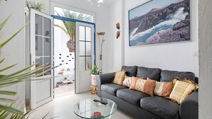 Un salon comprenant un canapé, une table basse en verre, une porte donnant sur l’extérieur et un grand tableau encadré accroché au mur.