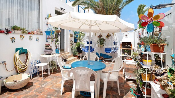 Une terrasse avec une table ronde, des chaises blanches et un fauteuil suspendu.