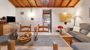 Una habitación acogedora con techo de madera, televisor, una mesa de comedor con sillas, un sofá y una lámpara de pared.