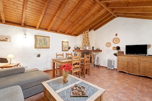 Ein gemütliches Wohnzimmer mit Holzbalkendecke, einem Essbereich mit Stühlen und Tisch, einer Couch, einem Fernseher und einem Kamin.