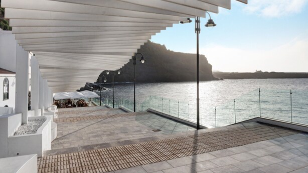 Terraza frente al mar con diseño moderno, que incluye una pérgola, asientos al aire libre y vistas al mar.