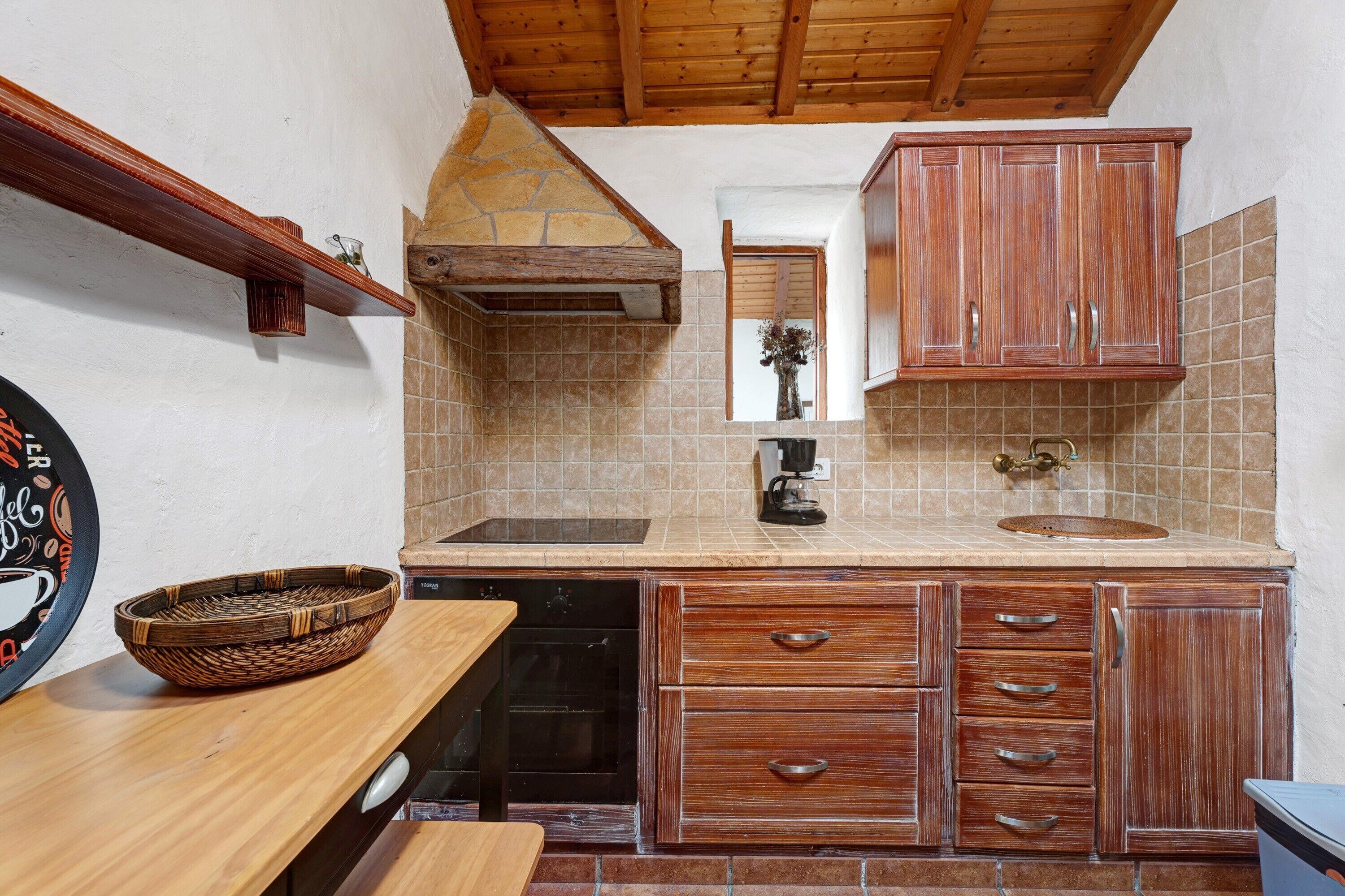 A kitchen with wooden cabinets, a stone chimney, a tiled backsplash, and a coffee maker.
