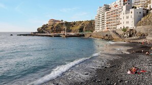 Una playa costera con un litoral rocoso, un muelle y edificios con balcones que dan al mar.
