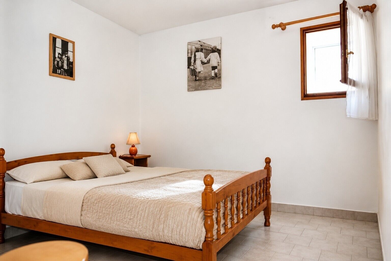 Un dormitorio con cama de madera, una mesita de noche con lámpara y dos fotografías enmarcadas en la pared.
