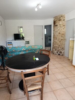 Un coin repas avec une table ronde, des chaises, un téléviseur posé sur un meuble, un canapé à motifs et un mur en pierre.