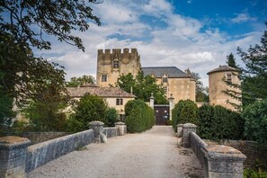 Un edificio con aspecto de castillo, con una torre central, rodeado de vegetación y un camino de grava.