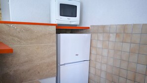 A compact kitchen with a microwave on top of a white refrigerator, a woven mat on the counter, and tiled walls. - Durance Apartment with Terrace and Garden (Allemagne-En-Provence)