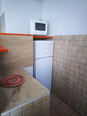 Una cocina compacta con un microondas sobre un refrigerador blanco, un tapete tejido en la encimera y paredes de azulejos.