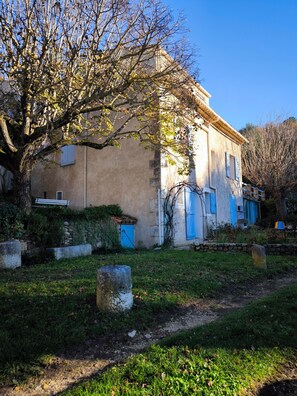 Um edifício rústico com fachada de pedra, uma grande árvore em primeiro plano e um céu azul claro.