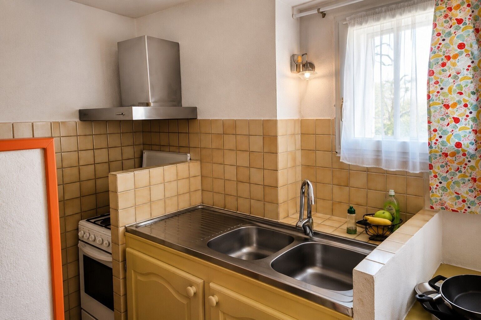 Une cuisine compacte équipée d’une cuisinière à gaz, d’un évier double et d’une hotte en acier inoxydable.