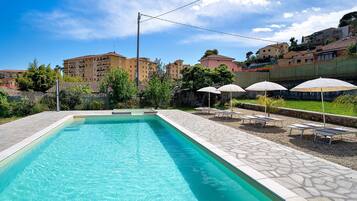 Una piscina con sillas de descanso y un deck de piedra, rodeada de edificios.