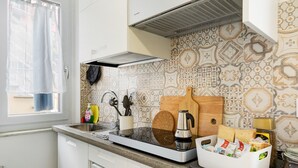 A kitchen with a built-in stove, a coffee maker, a bread box, and a window with a curtain. - Holiday Home 'Il Gattino Di Porto Appartamento 1' with Shared Pool, Wi-Fi and Air Conditioning (Imperia)