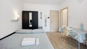 A hotel room with a bed, a desk, a chair, a table, a lamp, a clock, and a radiator. - Holiday Home 'Il Gattino Di Porto Appartamento 1' with Shared Pool, Wi-Fi and Air Conditioning (Imperia)