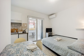 Ein kleines Hotelzimmer mit Bett, einem Tisch mit Schüssel und Löffel, einem Fernseher und einer Küchenzeile.
