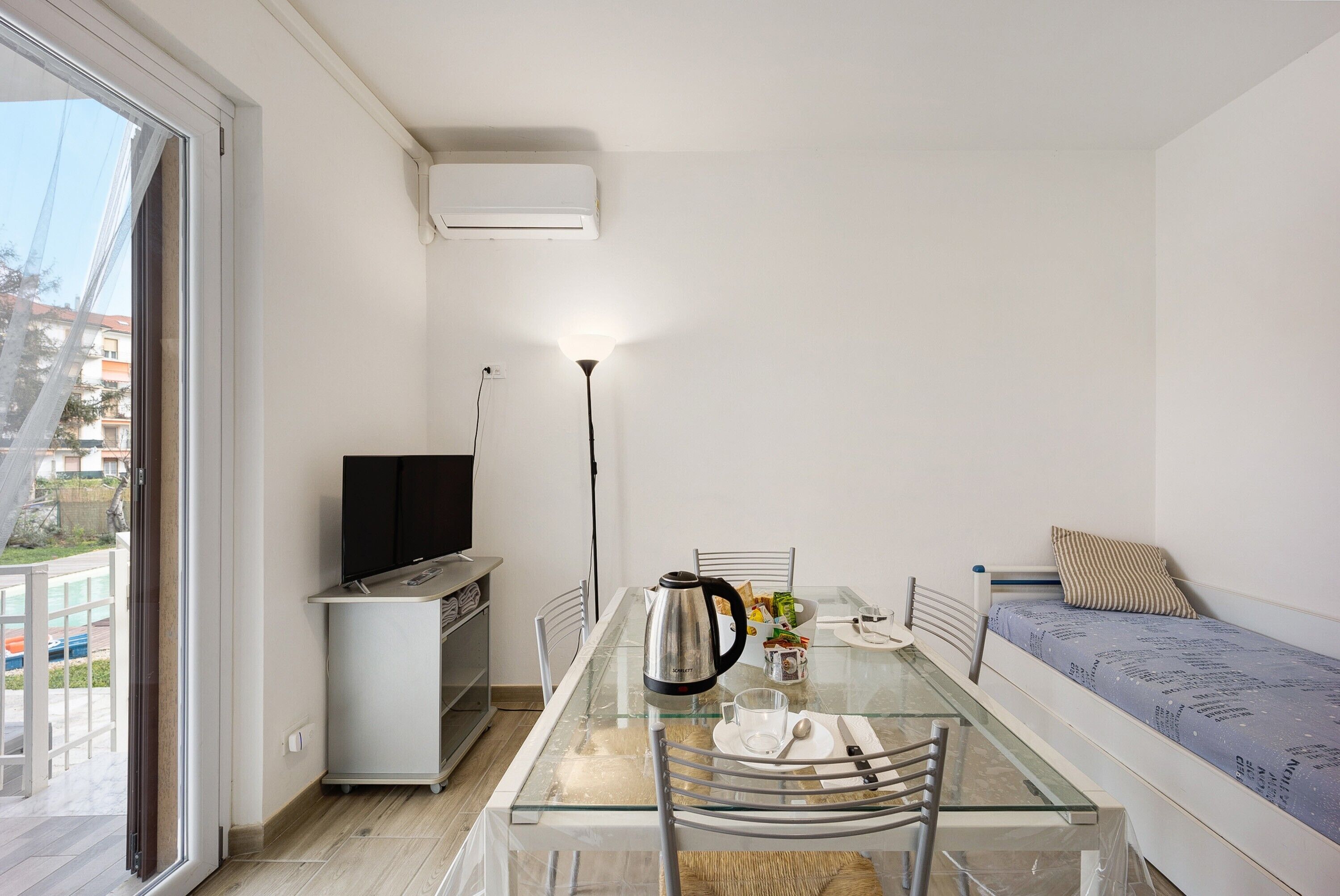 Una camera moderna con un tavolo in vetro, una TV, un bollitore, un letto e vista sugli edifici.