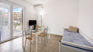 A room with a bed, a table with chairs, a TV, and a balcony with a view of buildings. - Holiday Home 'Il Gattino Di Porto Appartamento 2' with Shared Pool, Wi-Fi and Air Conditioning (Imperia)