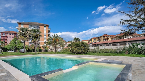 A swimming pool with a stone border, surrounded by buildings and greenery. - Holiday Home 'Il Gattino Di Porto Appartamento 2' with Shared Pool, Wi-Fi and Air Conditioning (Imperia)
