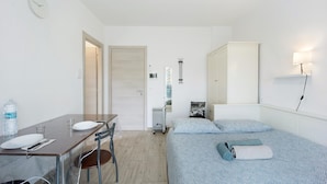 Une pièce comprenant un lit, une table avec des chaises, un radiateur et une horloge au mur.