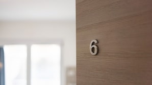 Gros plan d’une porte en bois sur laquelle figure un numéro de chambre, le chiffre « 6 », en métal.