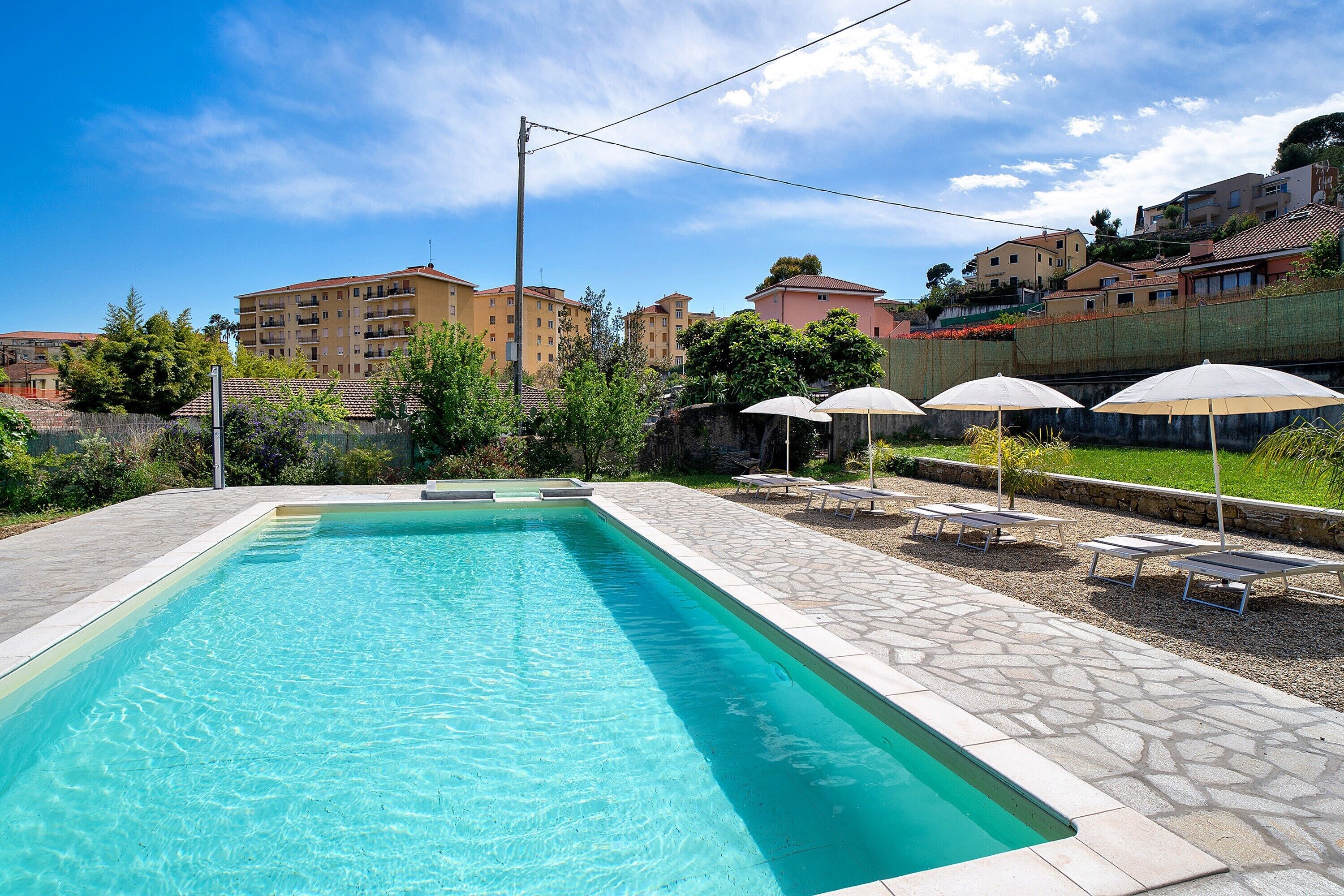 Une piscine dotée de chaises longues et d’une terrasse en pierre, entourée d’immeubles.