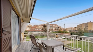 Un balcon avec une table et des chaises, une vue sur un quartier résidentiel et une piscine en arrière-plan.