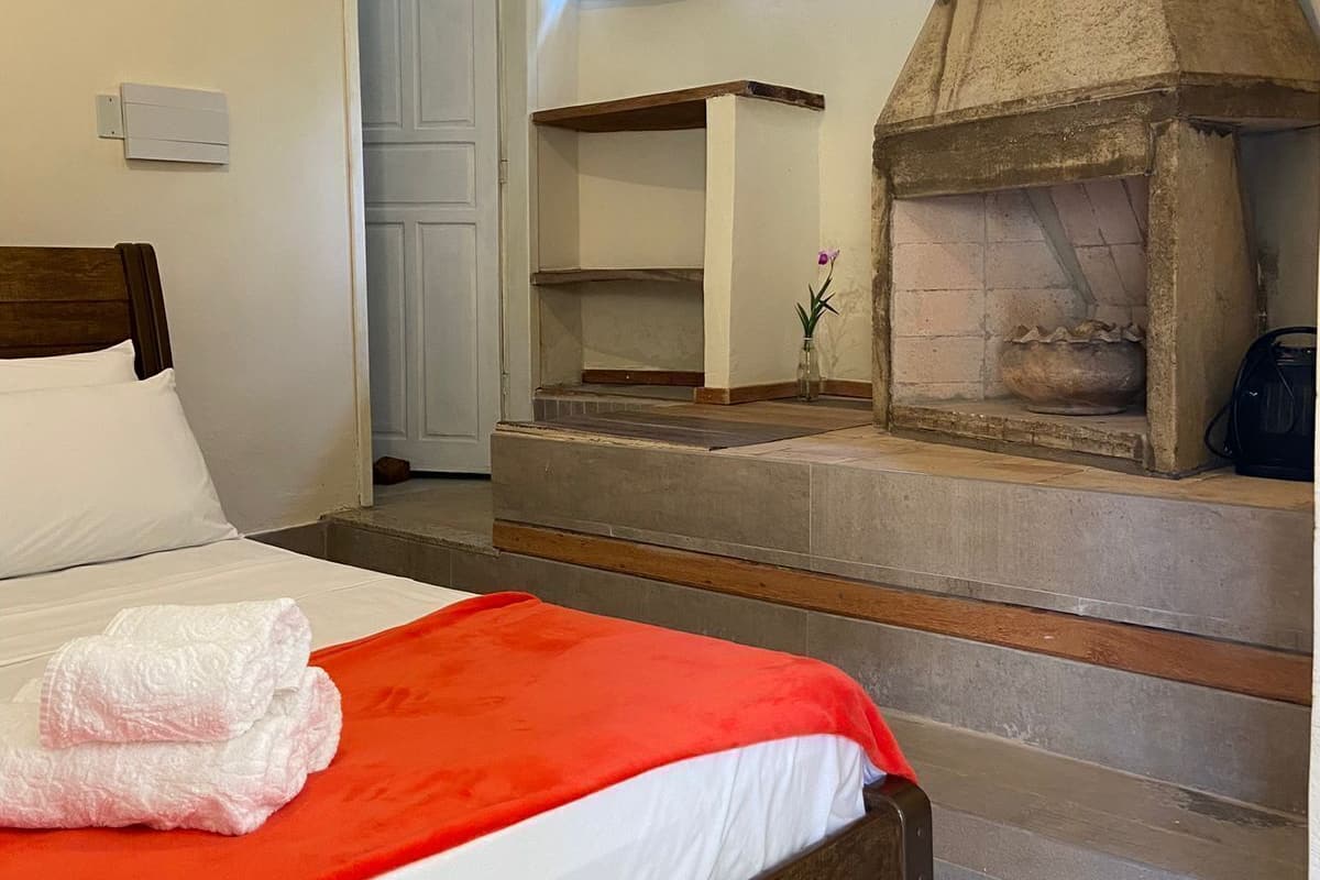 Ein Schlafzimmer mit einem Bett, einer roten Decke, einem Kamin aus Stein und einer Tür zu einem weiteren Raum.