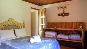 A bedroom with a bed, a wooden headboard, a shelf with towels, and a wall-mounted shelf with flowers.